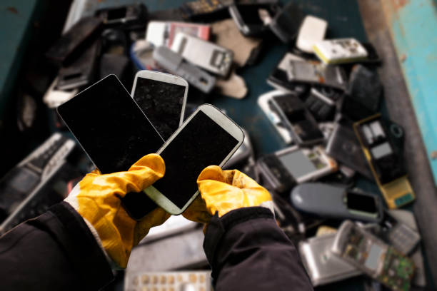 A person holding discarded smartphones with a pile of e-waste in the background, highlighting environmental concerns.